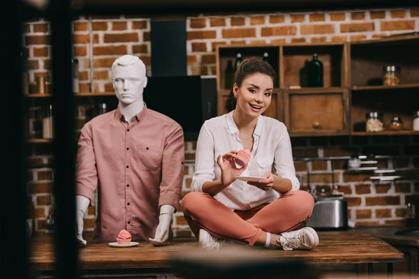 Mujer con cupcake sentado en la mesa con maniquí detrás, concepto de soledad - foto de stock