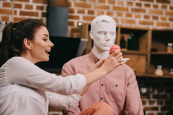 Mujer emocionada fingiendo alimentar maniquí con magdalena en casa, concepto de sueño relación perfecta - foto de stock