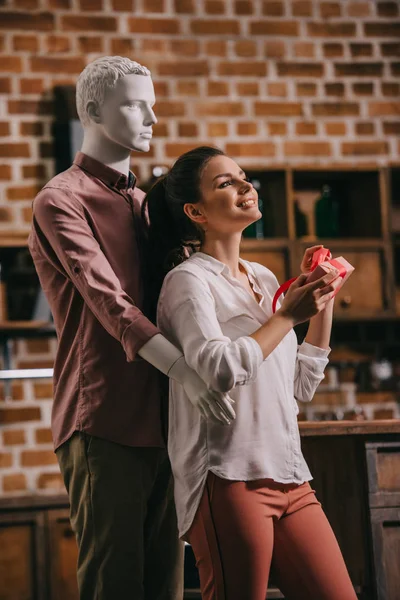 Young woman opening gift in hands with manikkin hugging her behind, perfect man dream concept — Stock Photo