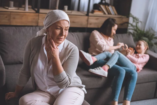 Kranke reife Frau im Halstuch schaut weg, während Familienmitglieder Spaß hinter sich haben — Stockfoto