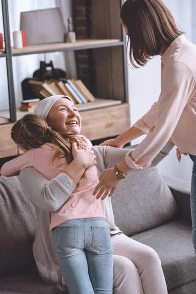 Mutter und Tochter besuchen kranke lächelnde Großmutter in Taschentuch — Stockfoto