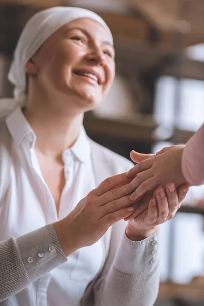 Cropped shot of child and smiling sick mature woman in kerchief holding hands — Stock Photo