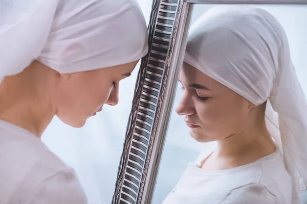 Side view of young sick woman in kerchief leaning at mirror — Stock Photo