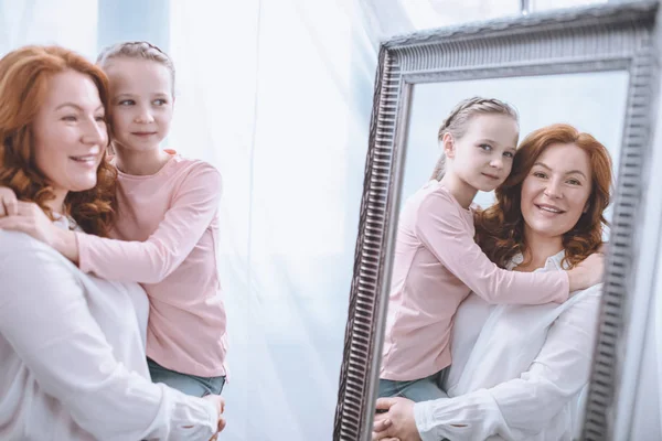 Счастливая бабушка и внучка обнимаются и смотрят в зеркало вместе — стоковое фото