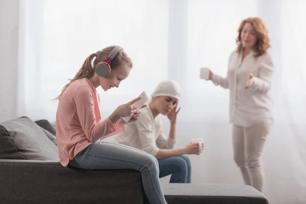 Child in headphones using digital tablet while sick mother and grandmother talking behind — Stock Photo