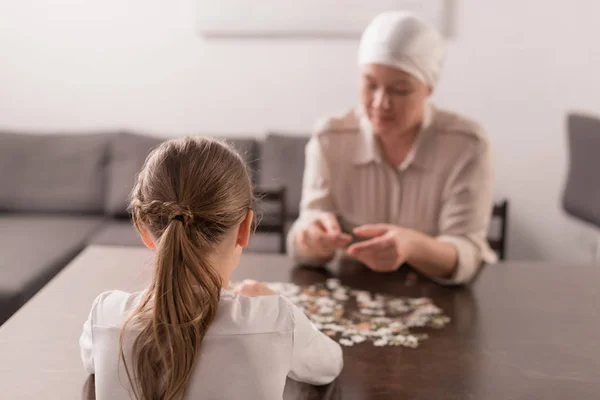 Vue arrière de l'enfant avec grand-mère malade dans le mouchoir jouant avec puzzle ensemble — Photo de stock