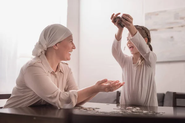 Fröhliches süßes kleines Kind mit kranker Großmutter im Halstuch, das mit Puzzle zusammen spielt — Stockfoto