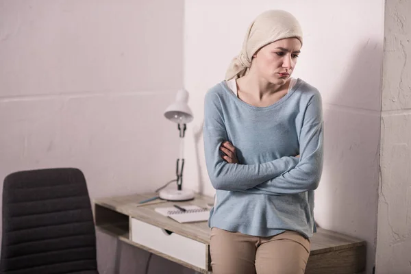 Bouleversé jeune femme malade en mouchoir assis avec les bras croisés et regardant loin — Photo de stock