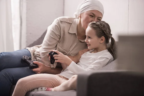 Grand-mère et petite-fille souriantes jouant avec des joysticks, concept de cancer — Photo de stock