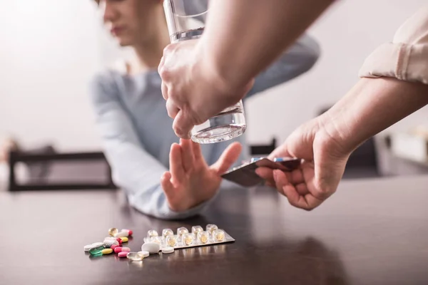 Recortado tiro de madre trayendo vaso de agua y medicina a enferma hija adulta - foto de stock