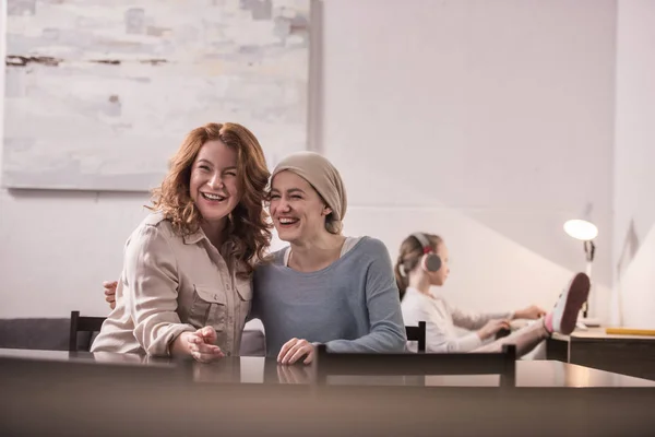 Feliz madre y enferma hija adulta en pañuelo riendo mientras están sentados juntos - foto de stock