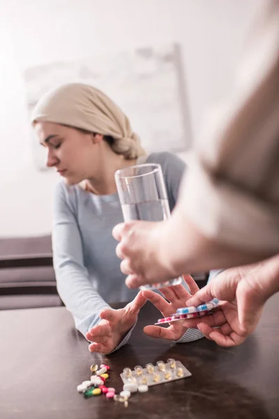 Selective focus of woman bringing glass of water and medicine to sick adult daughter in kerchief — Stock Photo