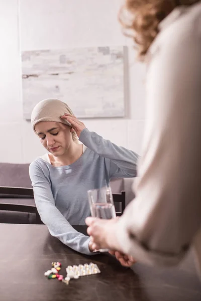 Cropped shot of woman bringing glass of water and medicine to sick adult daughter in kerchief — Stock Photo