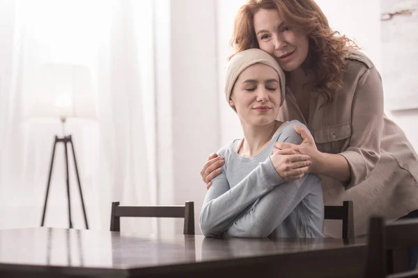 Reife Frau umarmt und unterstützt kranke lächelnde Tochter in Taschentuch — Stockfoto