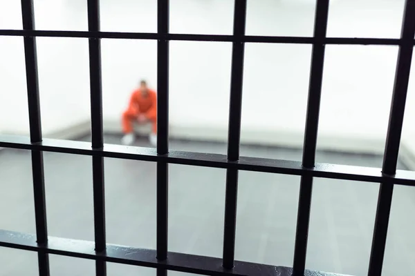 Prisionero sentado en el banco con las barras de la prisión en primer plano - foto de stock