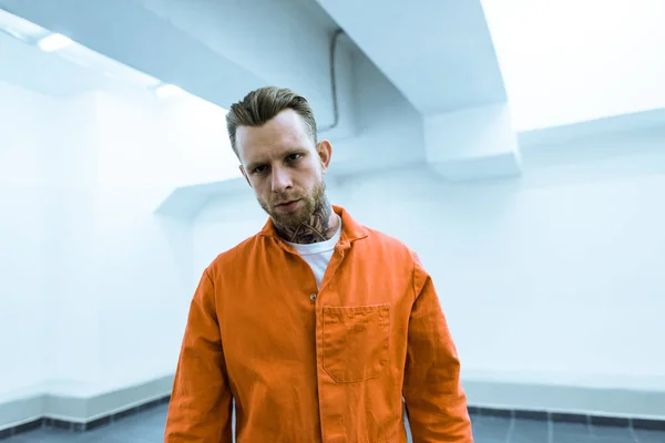 Prisionero tatuado en uniforme naranja mirando a la cámara - foto de stock