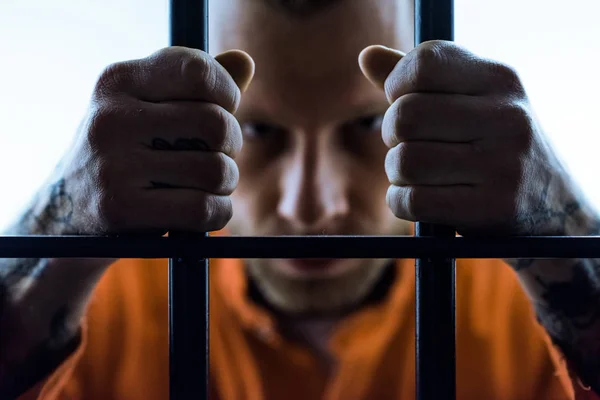 Злой заключенный держит тюремные решетки и смотрит в камеру — стоковое фото