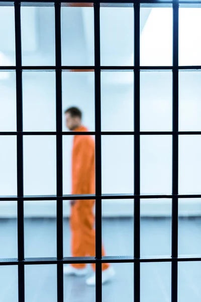 Vista lateral del prisionero parado detrás de las rejas - foto de stock