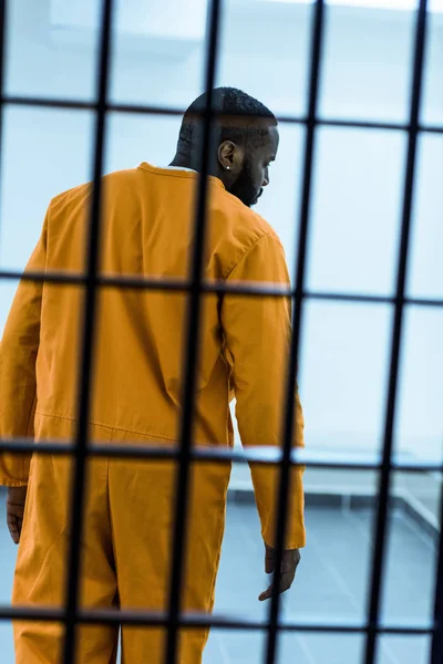 Rear view of african american prisoner behind prison bars — Stock Photo