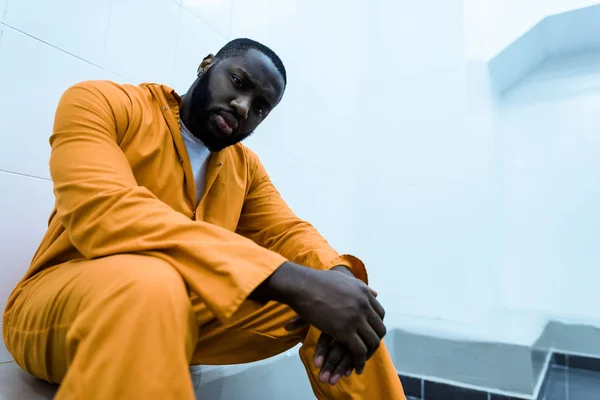 Vue du bas du prisonnier afro-américain assis sur le banc et regardant la caméra — Photo de stock