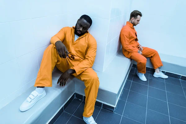 Visão de alto ângulo de prisioneiros multiculturais sentados em bancos na cela da prisão — Fotografia de Stock