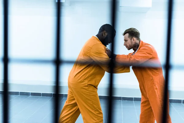 Vista lateral de prisioneros multiétnicos que luchan tras las rejas - foto de stock