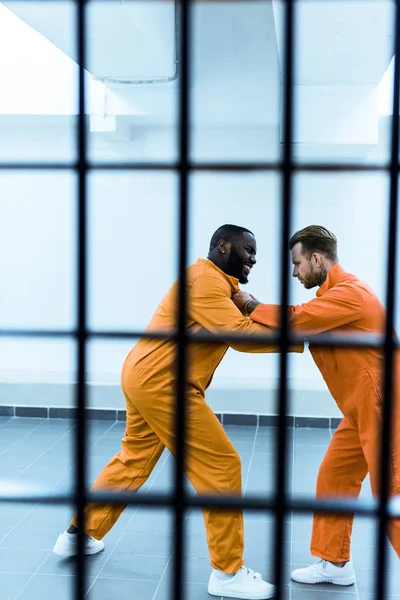 Вид сбоку на мультикультурных заключенных, угрожающих друг другу за решеткой — стоковое фото