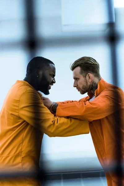 Side view of multicultural prisoners threatening each other and holding collars — Stock Photo