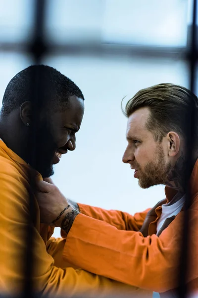 Side view of multiethnic prisoners threatening each other and holding collars — Stock Photo