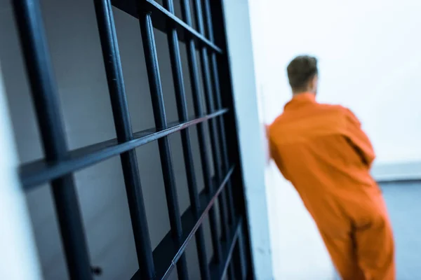Vista trasera del prisionero apoyado en la pared en la celda de la prisión - foto de stock