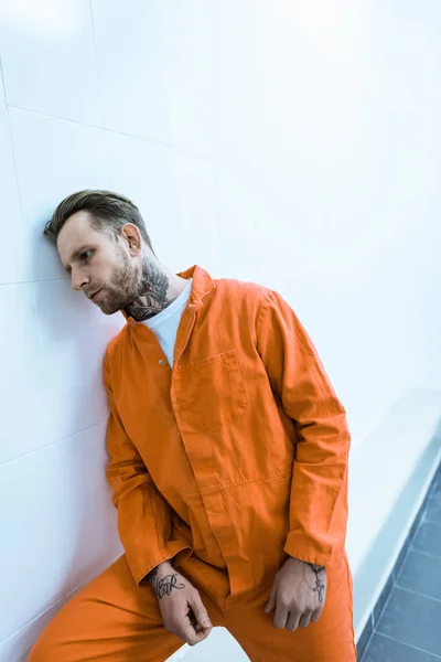 Татуированный заключенный, прислонившийся к стене тюремной камеры — стоковое фото