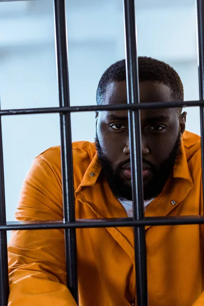 African american inmate looking at camera behind prison bars — Stock Photo