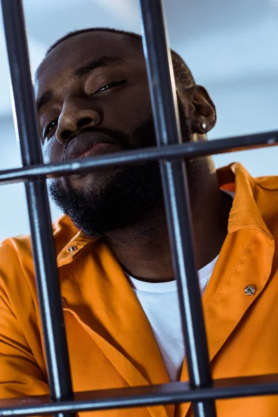 Criminel afro-américain regardant caméra derrière les barreaux de prison — Stock Photo