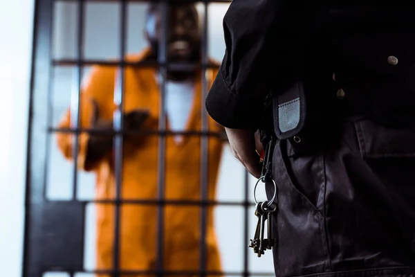 Immagine ritagliata della guardia di sicurezza in piedi vicino alle barre della prigione con le chiavi — Foto stock