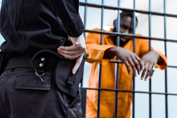 Cropped image of prison officer putting hand on gun near prison bars — Stock Photo