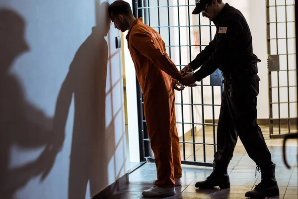 Vista lateral del oficial de la prisión con esposas en el prisionero - foto de stock