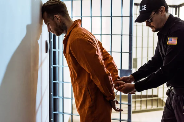 Vista lateral do oficial de prisão usando algemas em prisioneiro no corredor — Fotografia de Stock