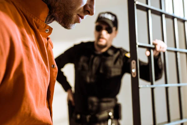 Cropped image of prison guard looking at criminal in prison cell — Stock Photo