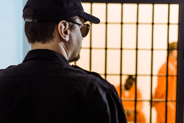 Rear view of prison officer standing near prison cell with criminals — Stock Photo