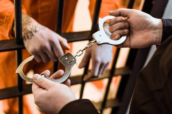 Cropped image of prison officer wearing handcuffs on prisoner — Stock Photo