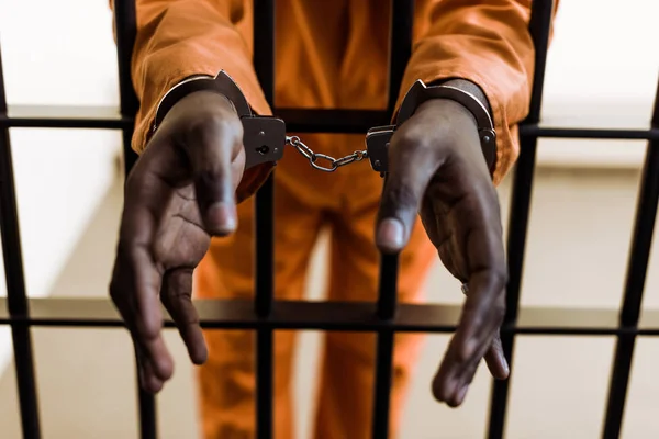 Cropped image of african american prisoner in handcuffs behind prison bars — Stock Photo