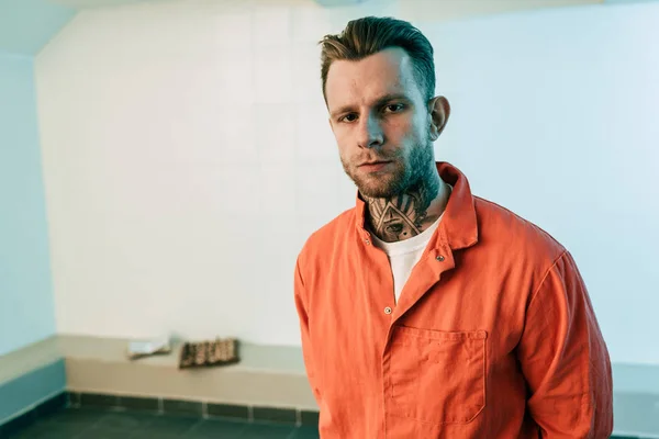 Tattooed prisoner looking at camera in prison cell — Stock Photo