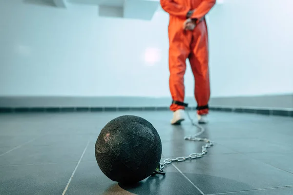 Back view of prisoner in orange uniform with weight tethered to leg — Stock Photo