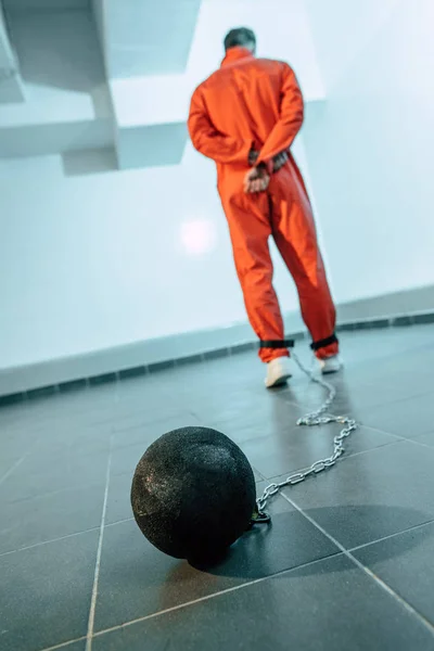 Vista trasera del prisionero en uniforme naranja con peso atado a la pierna - foto de stock