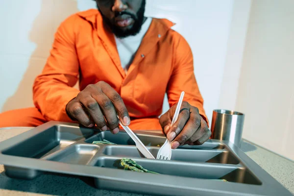 Imagen recortada de prisionero afroamericano comiendo en celda de prisión - foto de stock