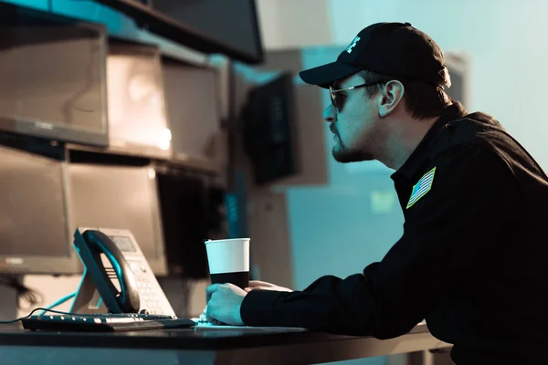 Side view of prison guard sitting with cup of coffee and monitoring people in jail — Stock Photo