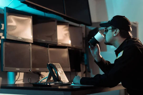 Prison guard drinking coffee at workspace and monitoring people in jail — Stock Photo