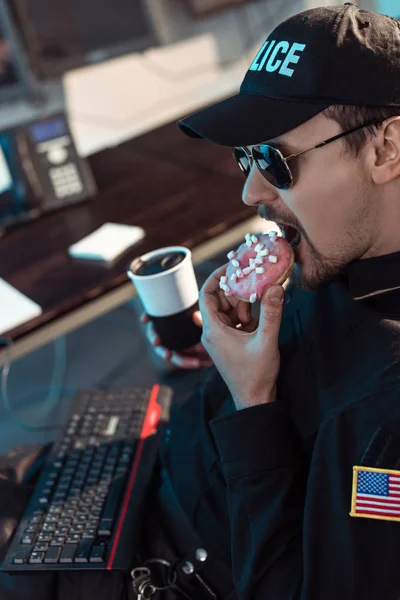 Guardia de la prisión comiendo donut y sosteniendo la taza de café - foto de stock