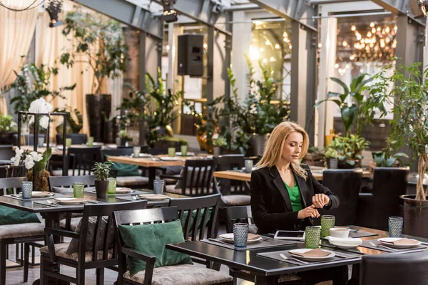 Bela mulher sentada à mesa e verificando o tempo no café — Fotografia de Stock