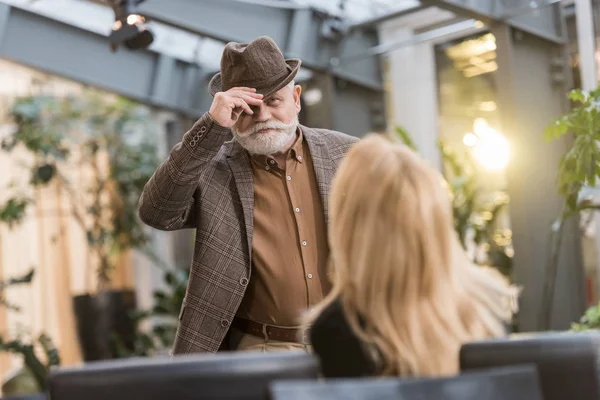 Seniorchef mit Hut blickt Frau am Tisch im Café an — Stockfoto